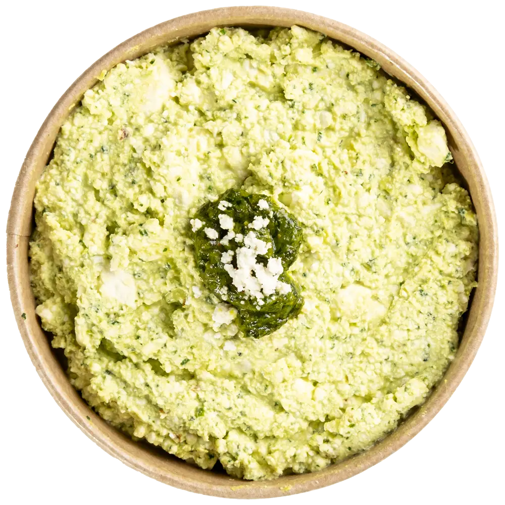 A bowl filled with creamy green dip topped with a dollop of darker green sauce and a sprinkle of white crumbled cheese. The smooth yet slightly chunky texture resembles mashed avocado and herbs, suggesting a flavorful blend, perfect for those exploring Mediterranean restaurants near me.